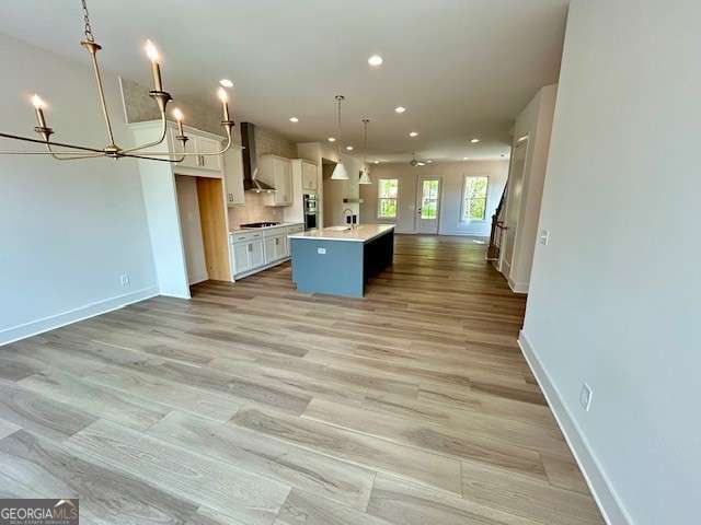 kitchen with white cabinets, light countertops, a kitchen island with sink, open floor plan, and a notable chandelier