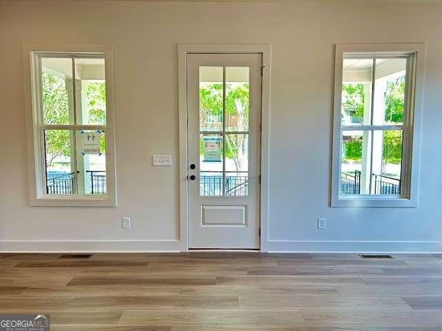 doorway to outside with wood finished floors, a healthy amount of sunlight, baseboards, and visible vents