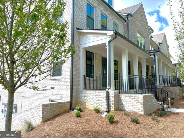view of side of home featuring covered porch and brick siding