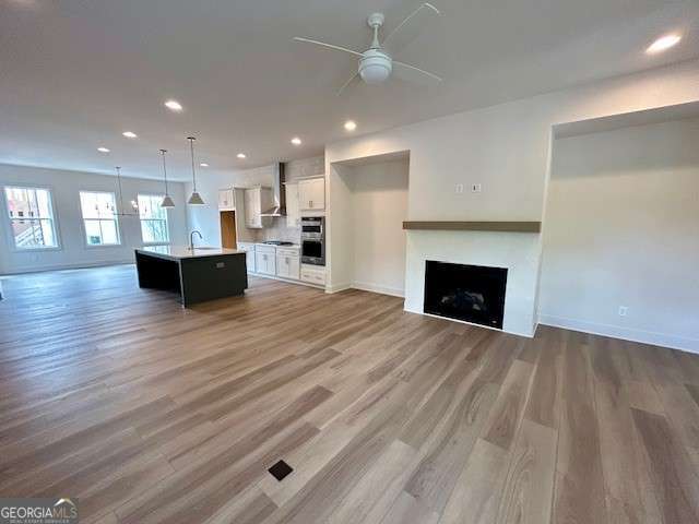 unfurnished living room featuring light wood finished floors, a ceiling fan, a sink, baseboards, and a fireplace