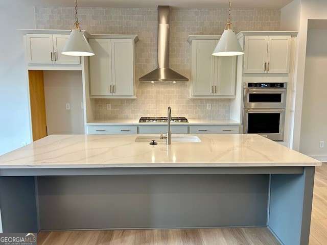 kitchen with stainless steel double oven, wall chimney range hood, a sink, a spacious island, and pendant lighting