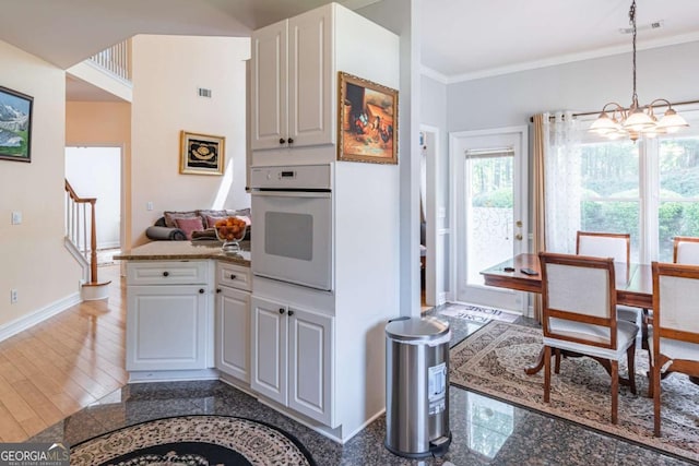 4319 Silver Peak Pkwy, Suwanee, GA 30024 - kitchen with crown molding, oven, white cabinetry, baseboards, and a notable chandelier