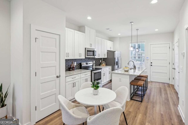 1095 Tucker Ave Unit 207, Atlanta, GA 30310 - kitchen with appliances with stainless steel finishes, an island with sink, light wood finished floors, backsplash, and white cabinets