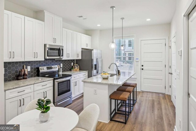 1095 Tucker Ave Unit 207, Atlanta, GA 30310 - kitchen featuring appliances with stainless steel finishes, wood finished floors, white cabinetry, a breakfast bar area, and a center island with sink
