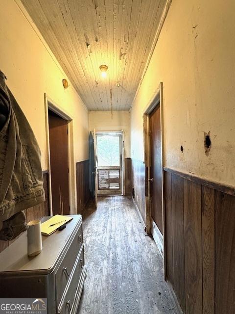hallway with wainscoting, wooden ceiling, wood finished floors, and wooden walls