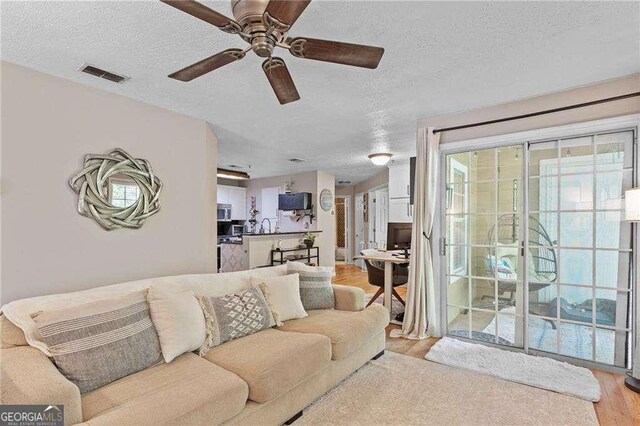 5566 River Heights Xing SE, Marietta, GA 30067 - living room featuring a textured ceiling, light wood-style flooring, visible vents, and ceiling fan