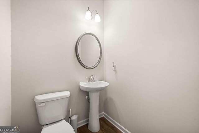 half bathroom with wood finished floors, baseboards, and toilet