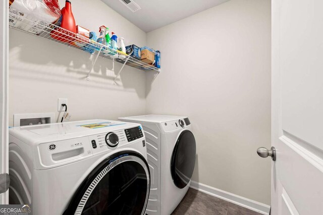 washroom with laundry area, visible vents, baseboards, dark tile patterned flooring, and separate washer and dryer