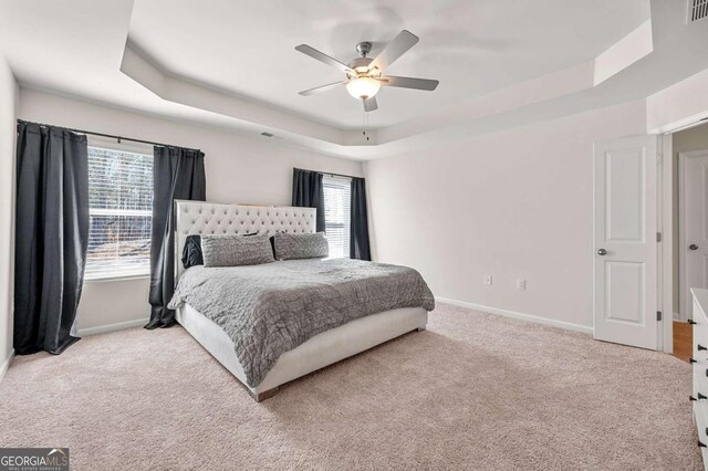 bedroom with baseboards, a tray ceiling, carpet, and multiple windows