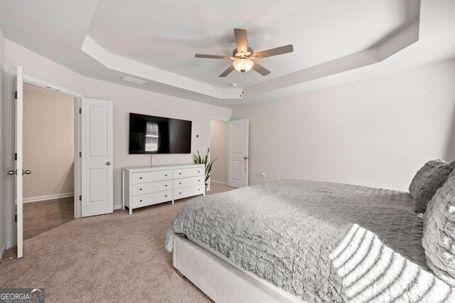 carpeted bedroom featuring ceiling fan, baseboards, and a tray ceiling