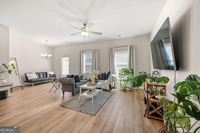 living area with light wood-style floors and ceiling fan with notable chandelier