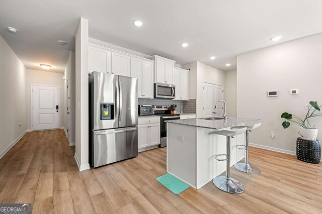 kitchen featuring white cabinets, stainless steel appliances, light wood-style flooring, a sink, and a breakfast bar area