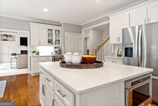 kitchen featuring white cabinets, crown molding, appliances with stainless steel finishes, a center island, and wood finished floors