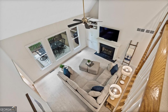 carpeted living room with visible vents, a fireplace with flush hearth, ceiling fan, and high vaulted ceiling