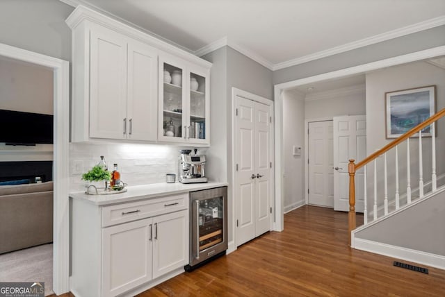 bar featuring decorative backsplash, crown molding, wood finished floors, wine cooler, and stairs