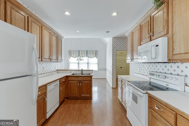 kitchen with white appliances, wallpapered walls, a sink, a peninsula, and light countertops