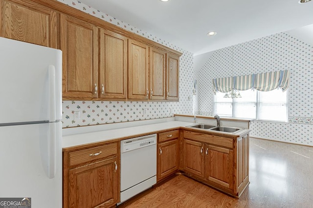 kitchen with white appliances, wallpapered walls, a sink, brown cabinets, and light countertops