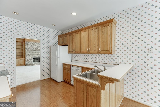 kitchen with wallpapered walls, white appliances, light wood-style flooring, a peninsula, and light countertops