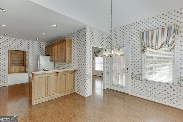 kitchen with wallpapered walls, freestanding refrigerator, light wood-style flooring, a peninsula, and light countertops