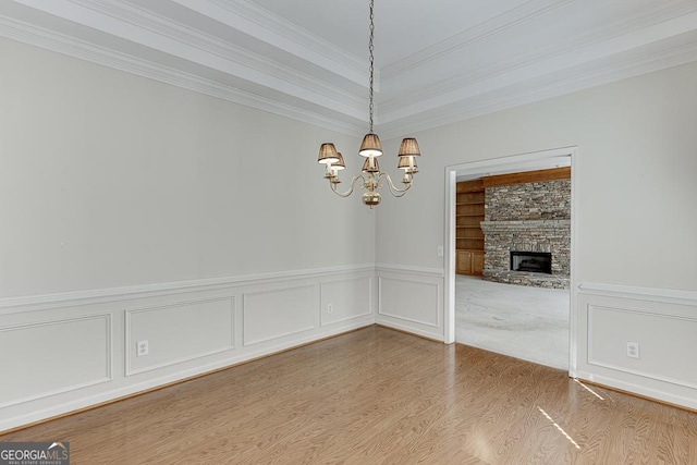 unfurnished dining area with a chandelier, wood finished floors, ornamental molding, a fireplace, and wainscoting