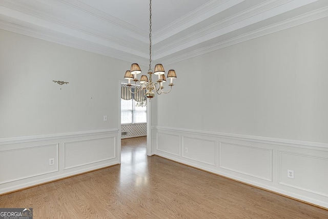 unfurnished dining area with a chandelier, wood finished floors, a decorative wall, crown molding, and a wainscoted wall