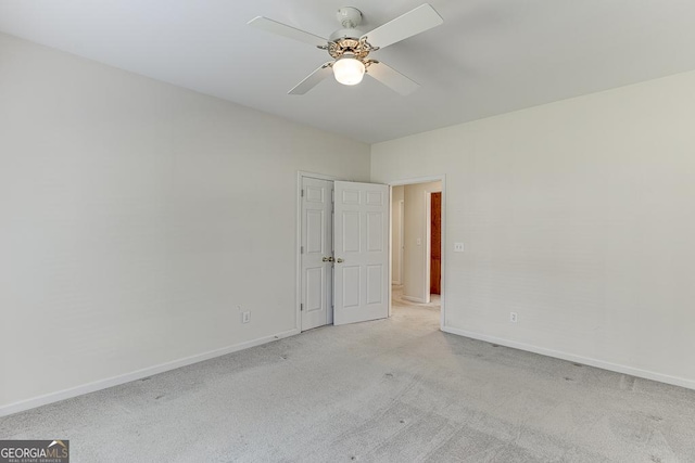 spare room with light carpet, a ceiling fan, and baseboards