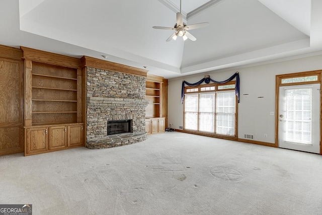 unfurnished living room with ceiling fan, a raised ceiling, plenty of natural light, a stone fireplace, and ornamental molding