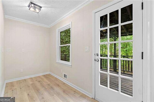 doorway to outside featuring a textured ceiling, light wood-style flooring, baseboards, ornamental molding, and visible vents