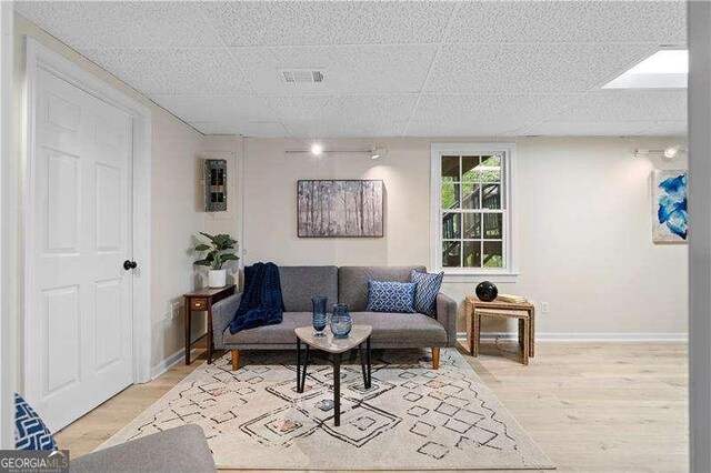 living room featuring light wood-style floors, a paneled ceiling, visible vents, and baseboards