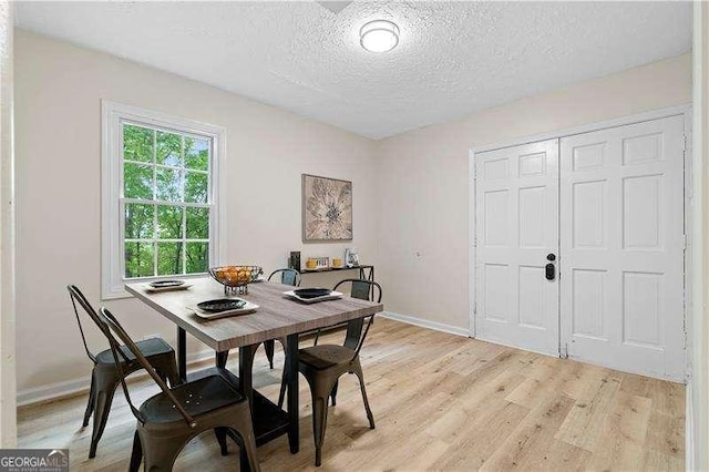 dining room featuring baseboards, a textured ceiling, and light wood-type flooring