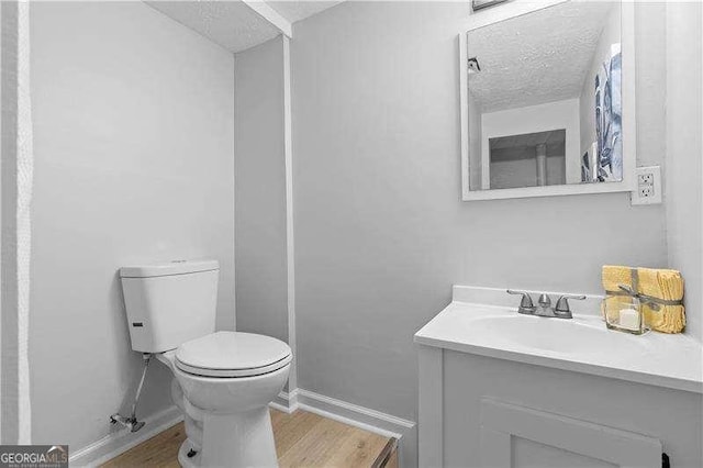 half bathroom with a textured ceiling, toilet, baseboards, wood finished floors, and vanity