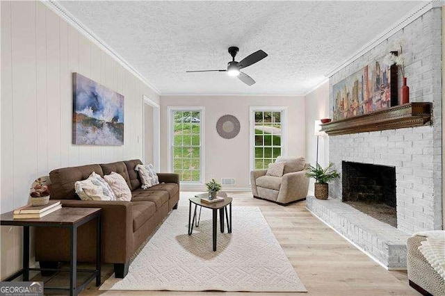 living room featuring crown molding, a brick fireplace, light wood finished floors, and ceiling fan