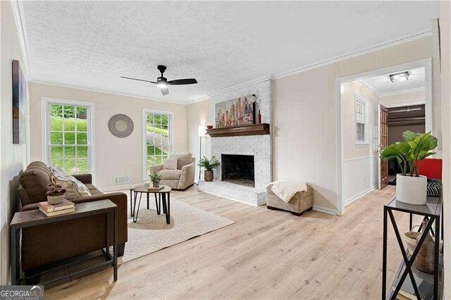 living area with light wood-type flooring, baseboards, ceiling fan, crown molding, and a fireplace
