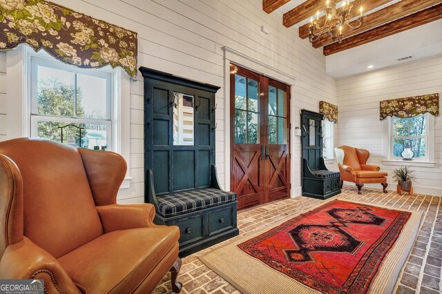 sitting room featuring a healthy amount of sunlight, brick floor, wooden walls, and an inviting chandelier