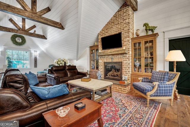 living area featuring visible vents, vaulted ceiling with beams, hardwood / wood-style flooring, and a brick fireplace