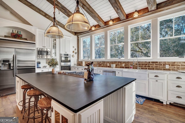 kitchen with dark countertops, a sink, white cabinets, and built in appliances