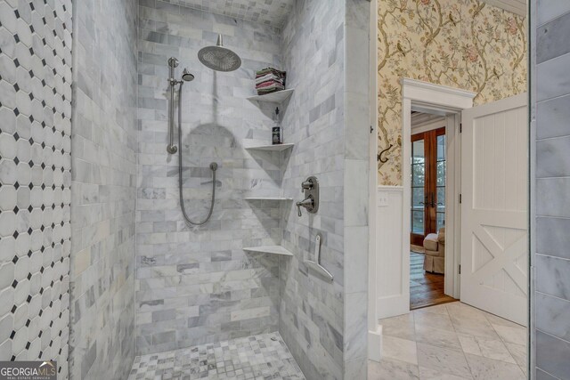 bathroom featuring a tile shower, wallpapered walls, and wainscoting