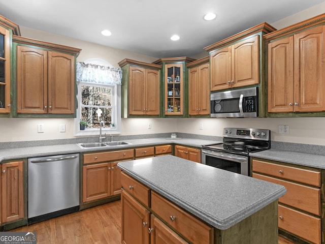 kitchen featuring appliances with stainless steel finishes, a sink, light wood finished floors, glass insert cabinets, and a center island
