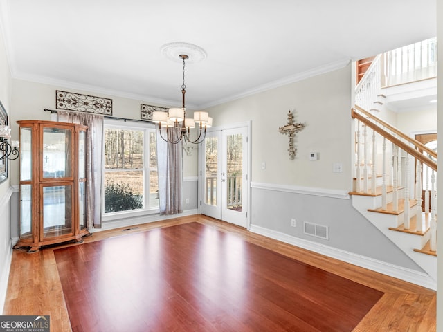 unfurnished dining area with a chandelier, stairs, wood finished floors, ornamental molding, and baseboards