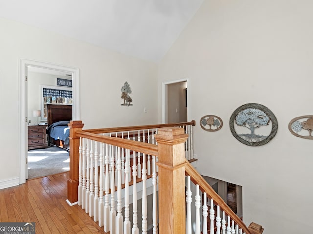 hallway with high vaulted ceiling, light wood-style flooring, an upstairs landing, and baseboards