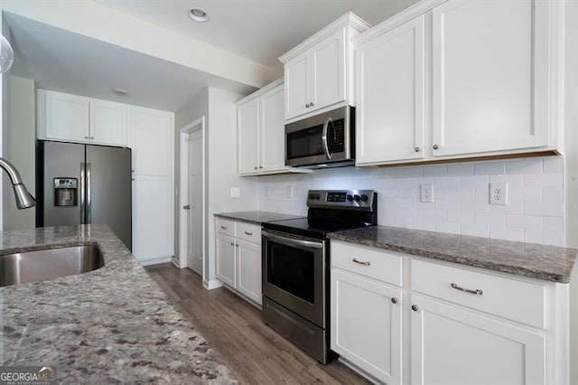 kitchen with appliances with stainless steel finishes, dark wood-style flooring, backsplash, white cabinets, and light stone counters
