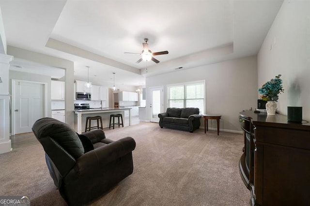 living room with a raised ceiling, light colored carpet, ceiling fan, and baseboards