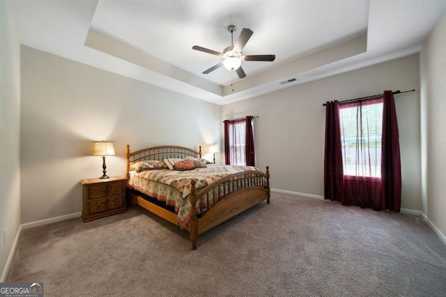 carpeted bedroom featuring baseboards, a tray ceiling, and ceiling fan