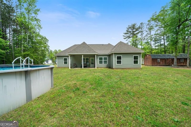 rear view of house with a storage unit, an outdoor structure, a lawn, and an outdoor pool