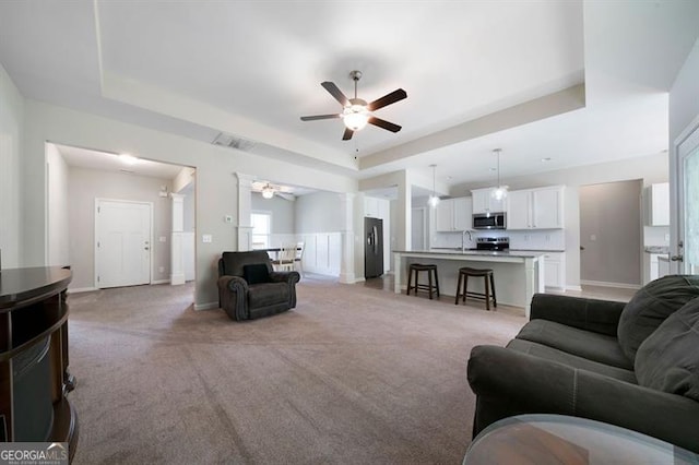 living room featuring a tray ceiling, a ceiling fan, light carpet, and baseboards