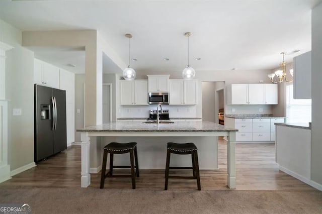 kitchen featuring stainless steel microwave, fridge with ice dispenser, a sink, a chandelier, and white cabinets