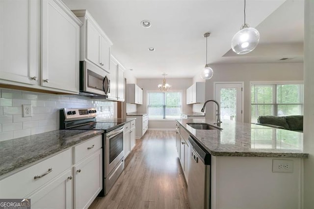 kitchen with appliances with stainless steel finishes, a sink, light wood finished floors, decorative backsplash, and a chandelier