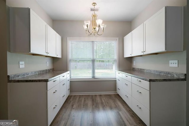 kitchen featuring a chandelier, wood finished floors, white cabinets, baseboards, and dark countertops