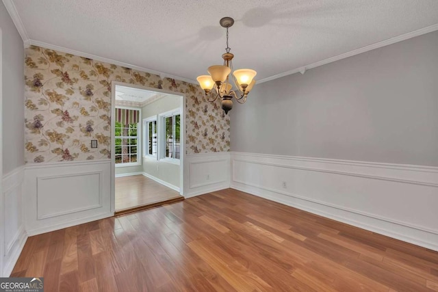 unfurnished dining area featuring a chandelier, wood finished floors, ornamental molding, and wainscoting