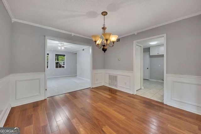 unfurnished dining area featuring ornamental molding, wood finished floors, a chandelier, and a wainscoted wall